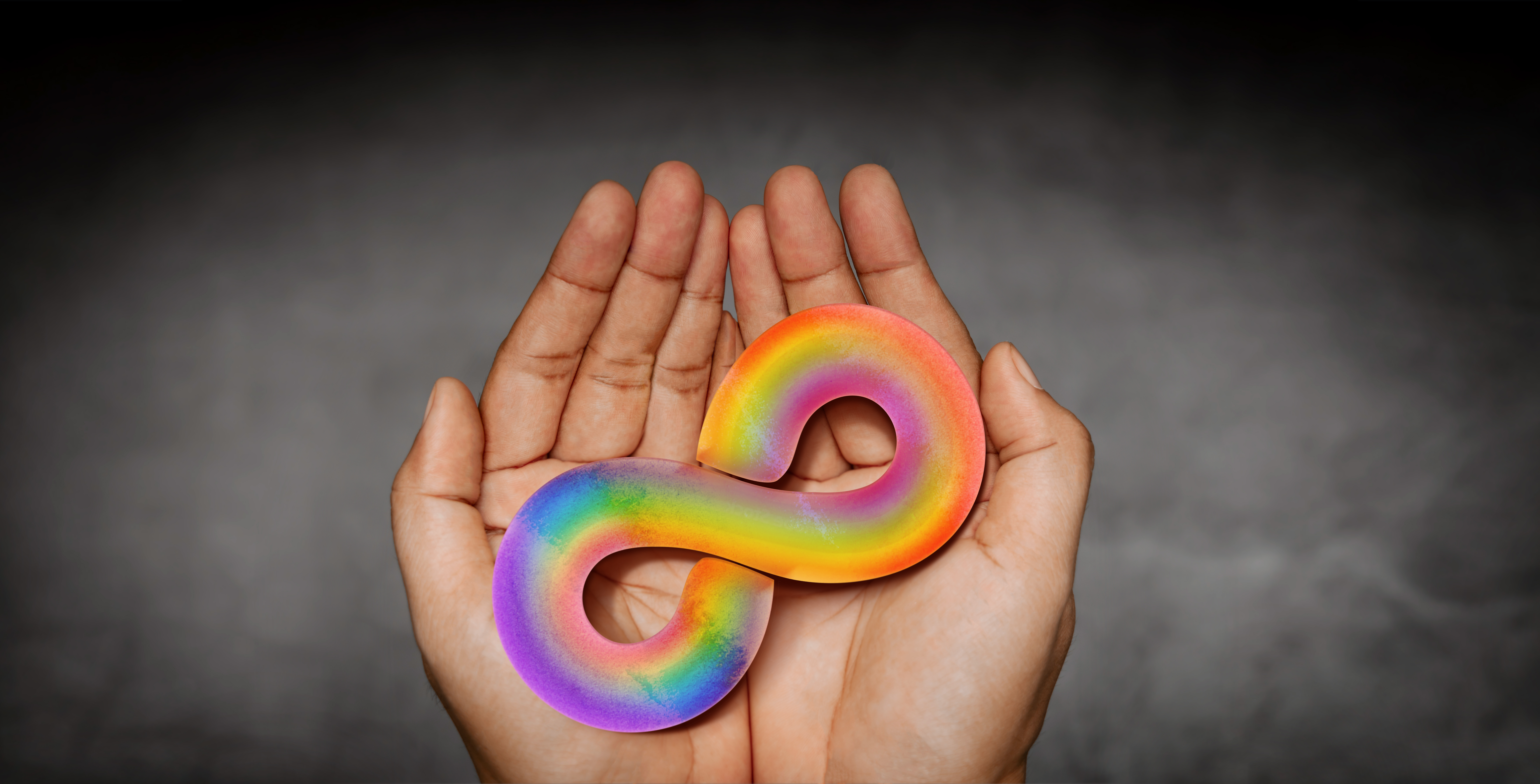 hands holding an autism awareness rainbow infinity symbol