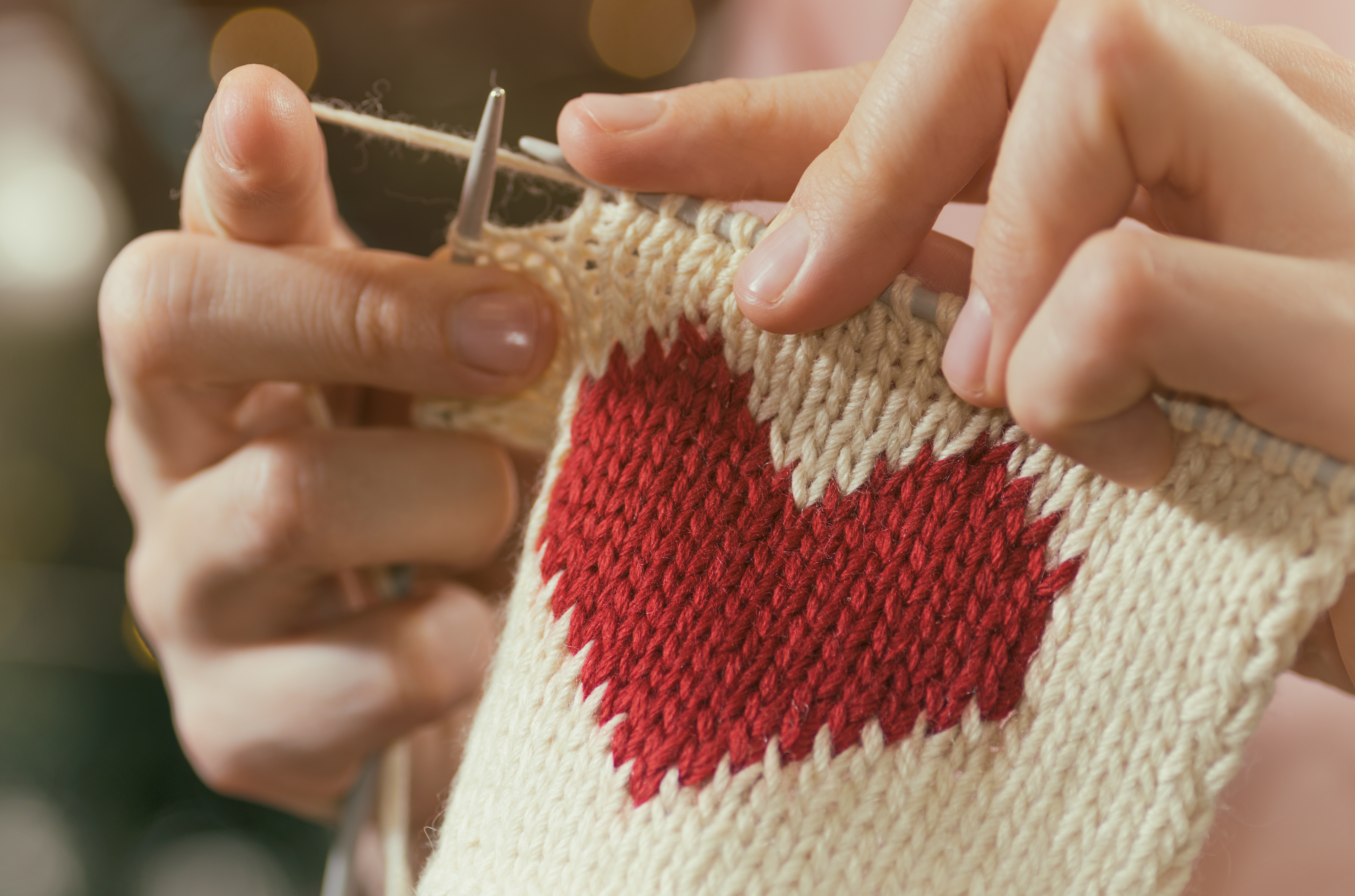 A person's hands knitting a design of a red heart on a white background