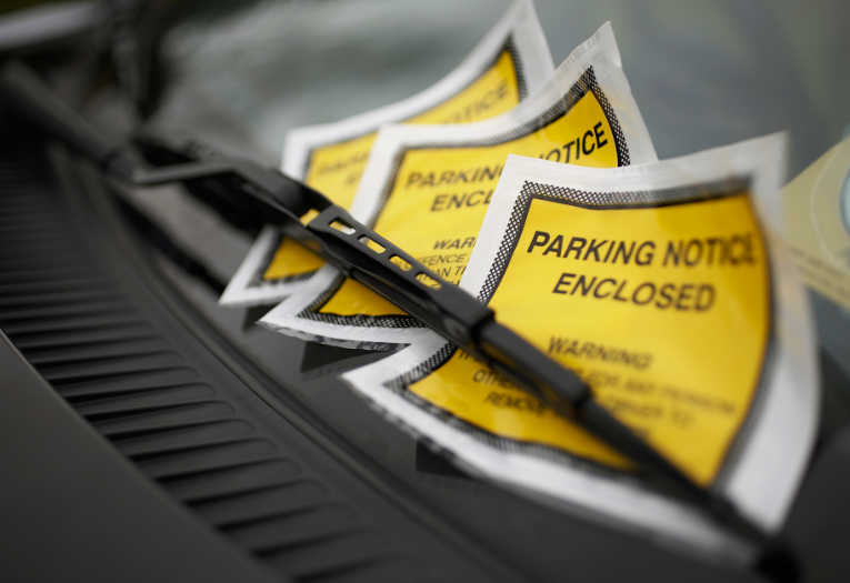 Image depicts three parking charge notices under a windscreen wiper of a car.