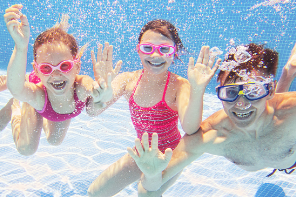 A dad and two children wearing goggles and swimming underwater in a pool