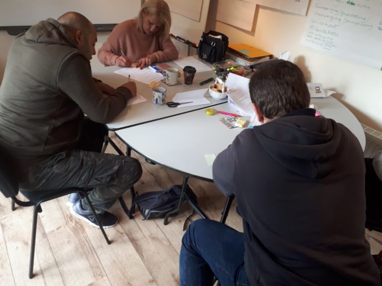 Three adults working at a table, writing on pieces of paper