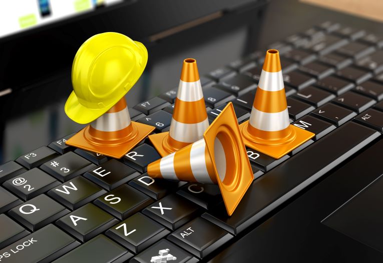 Image shows four orange cones and a yellow maintenance hat on a laptop keyboard.