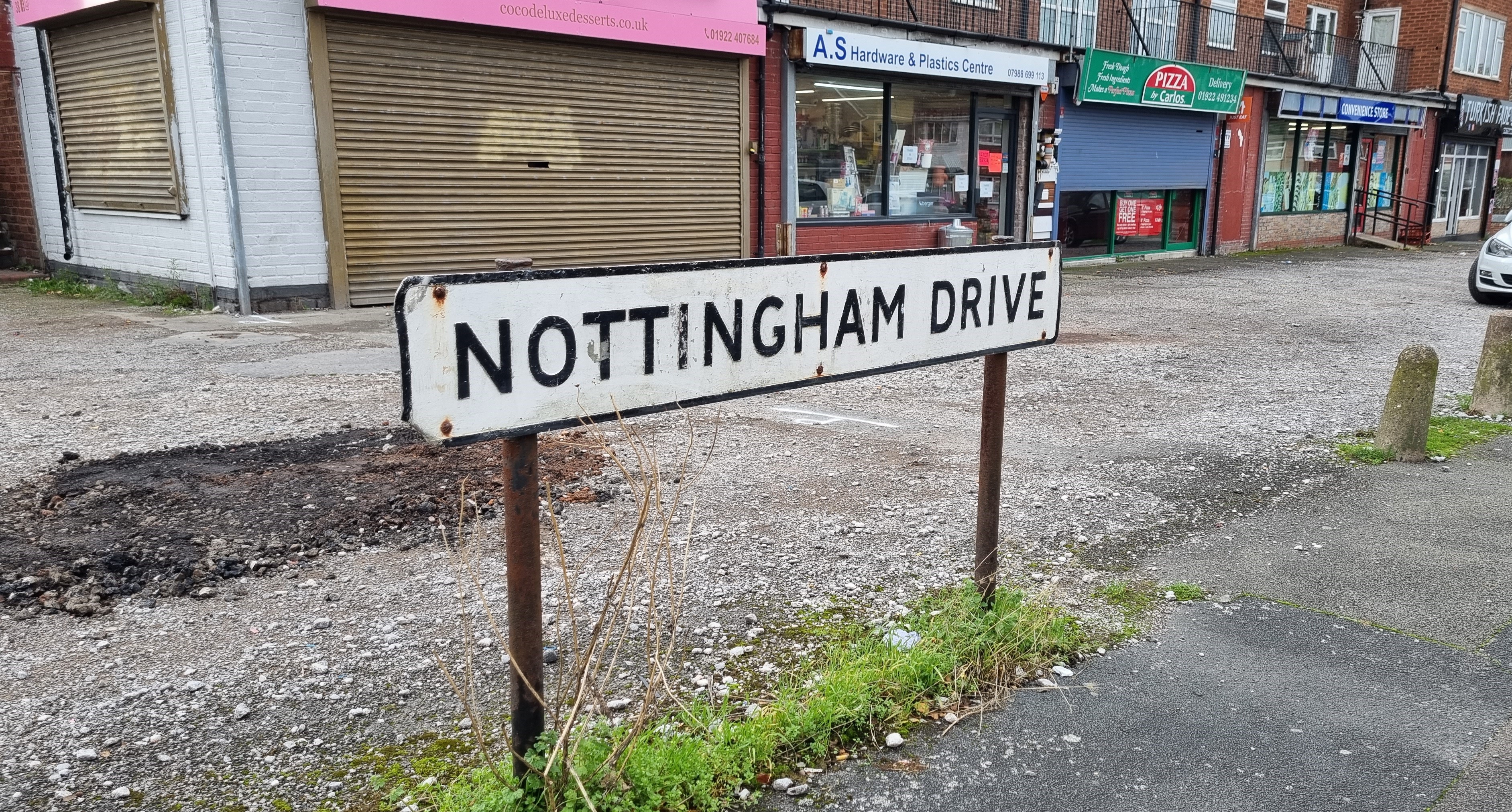 Street sign that reads Nottingham Drive, situated in front of a shopping area with carpark