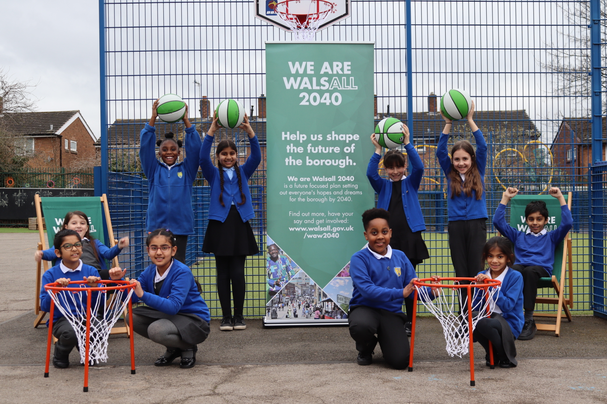 Pupils at Delves Junior School sitting in front of a basketball court holding basketballs