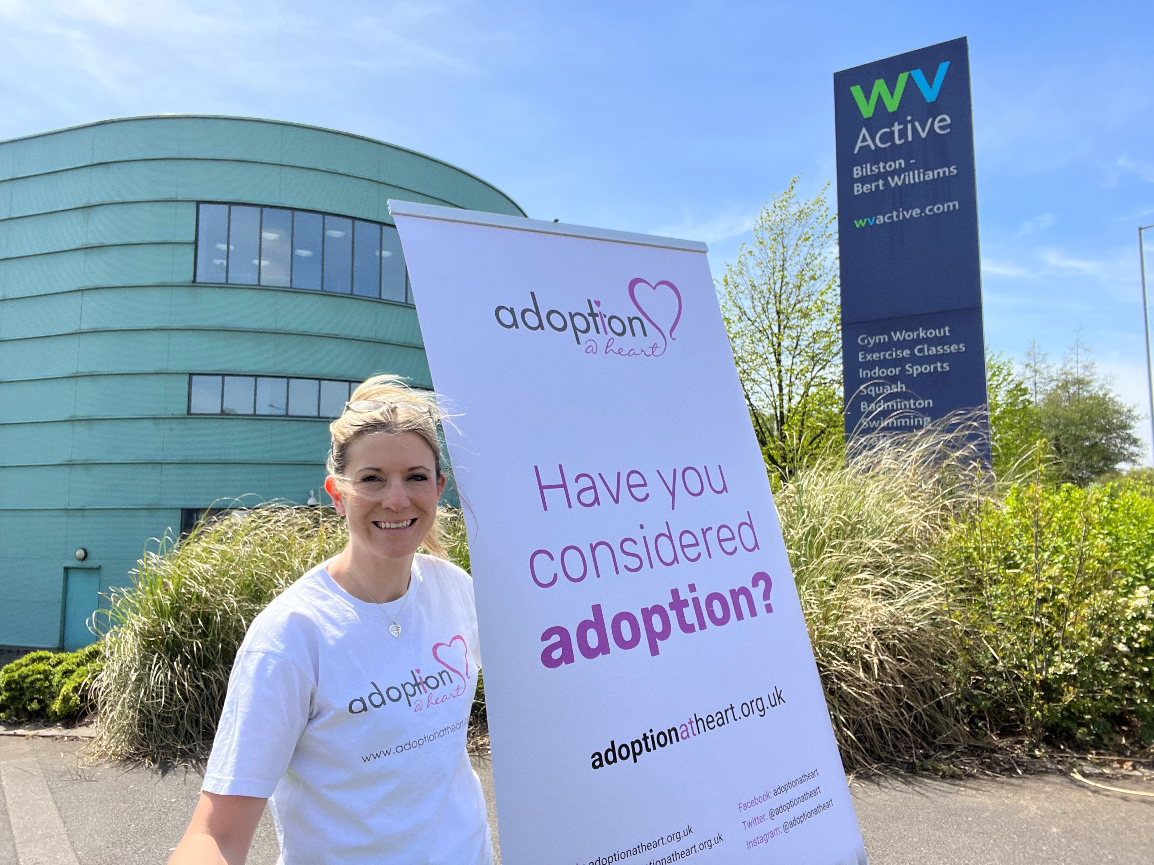 Image of lady holding adoption at heart banner outside Bert Williams Leisure centre