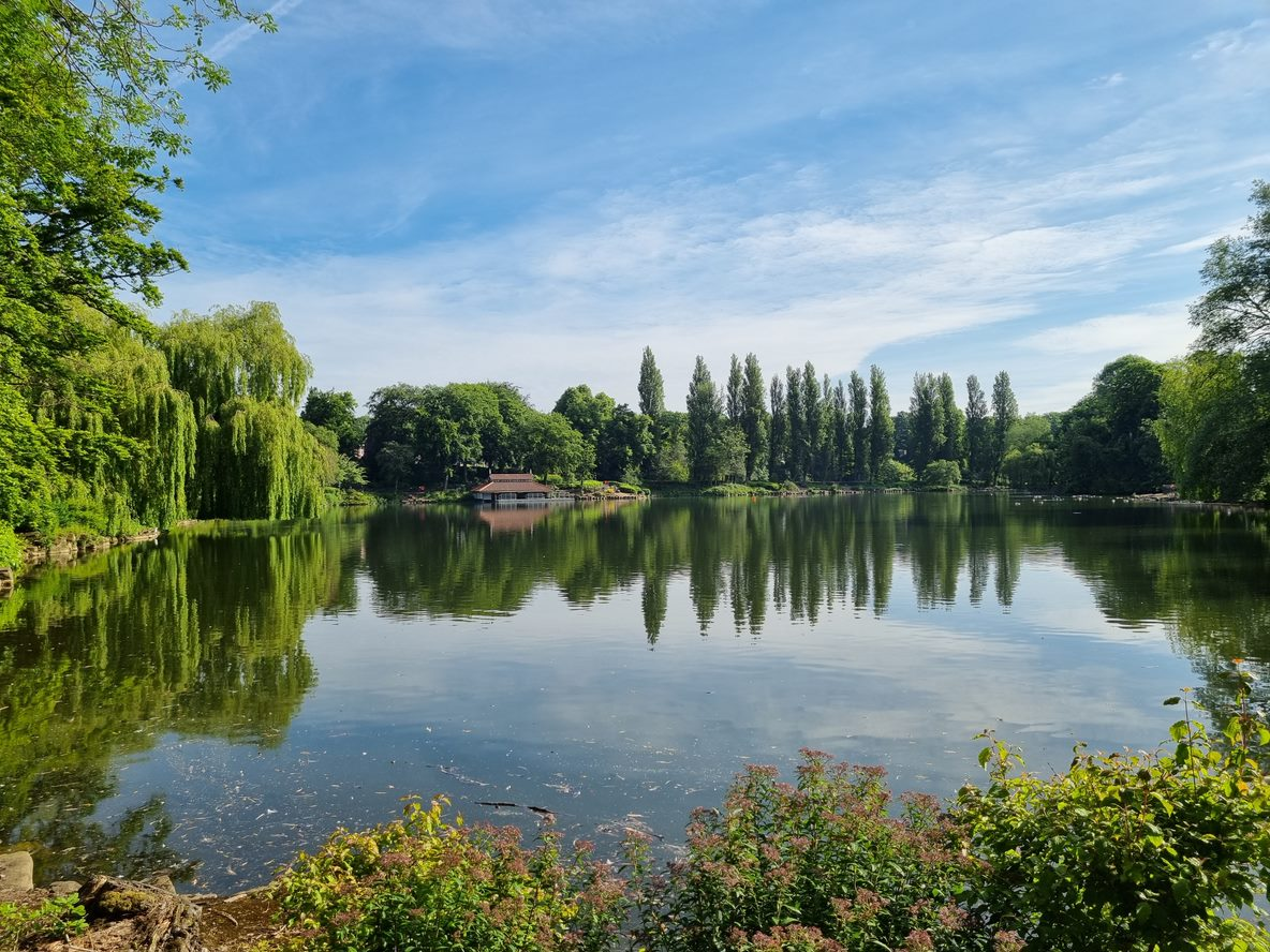 Image depicts the Walsall Arboretum lake showing the boathouse on a sunny day.
