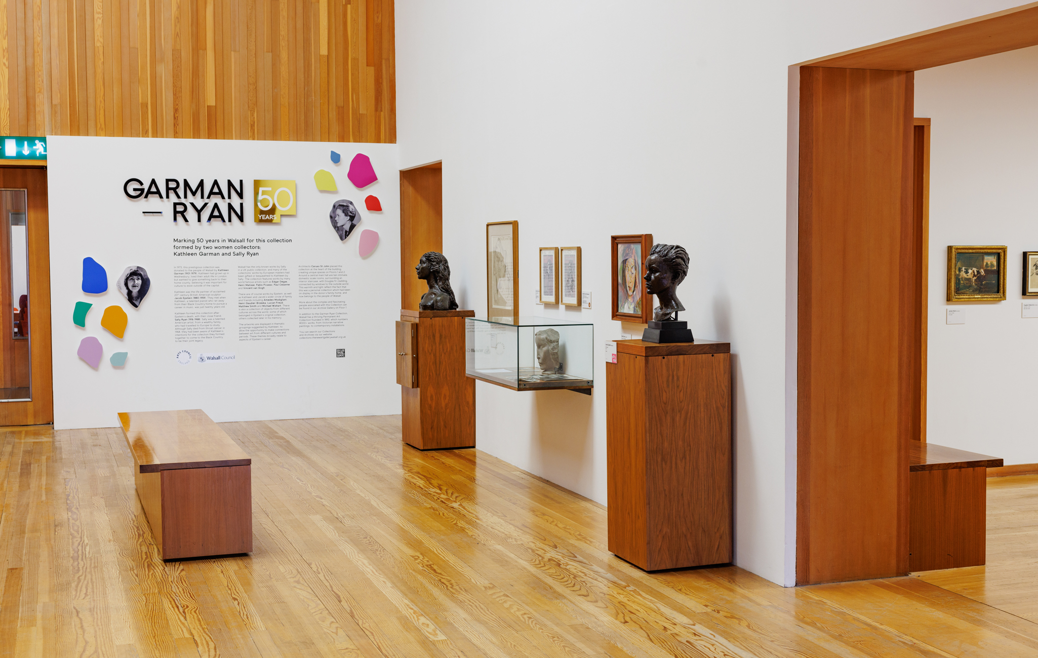 An view of The New Art Gallery Walsall's Garman Ryan Collection featuring sculptures of the co-founders Kathleen Garman and Sally Ryan as well as other wall-based artworks.