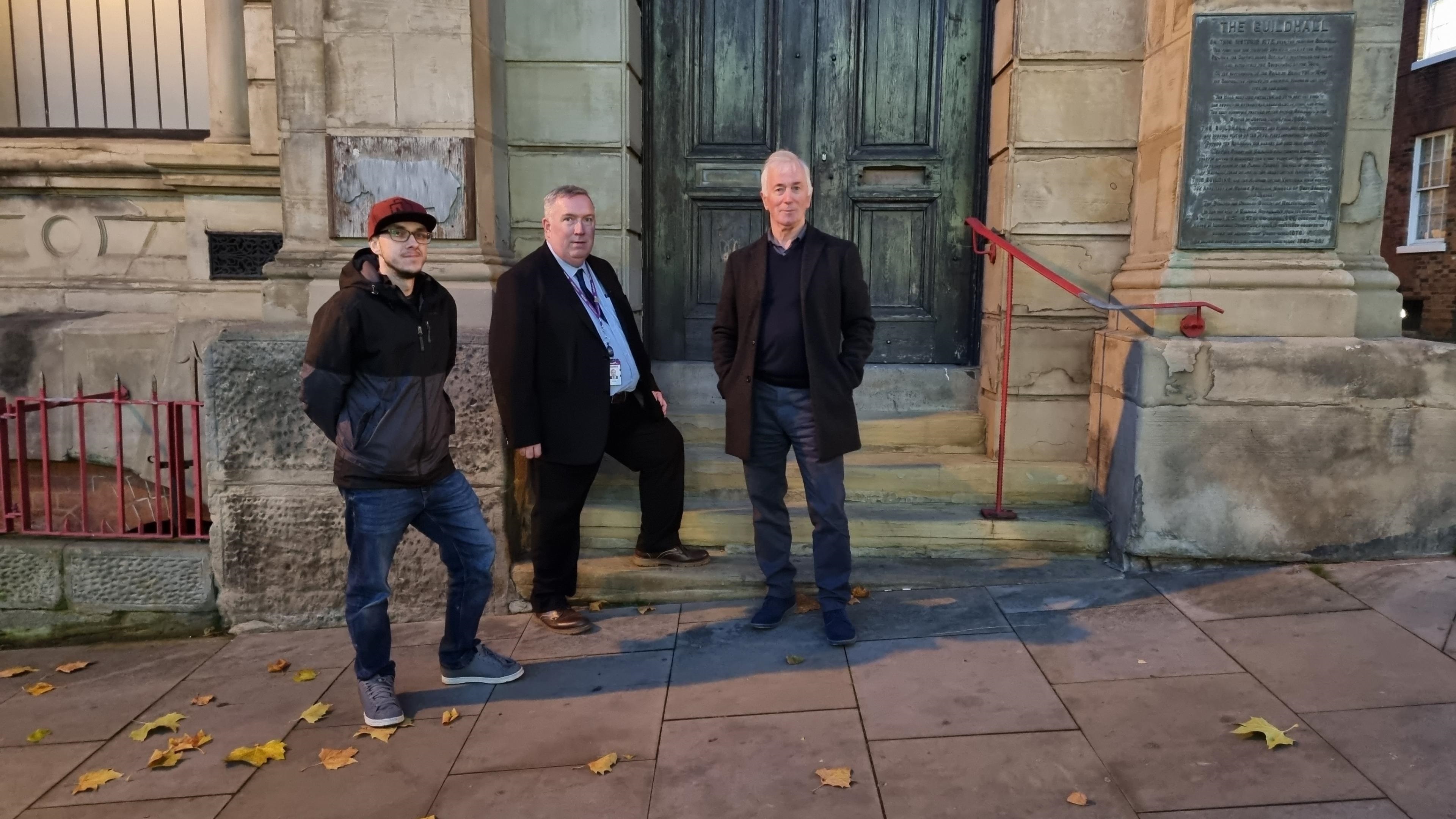 Three men standing together on the steps outside a building 