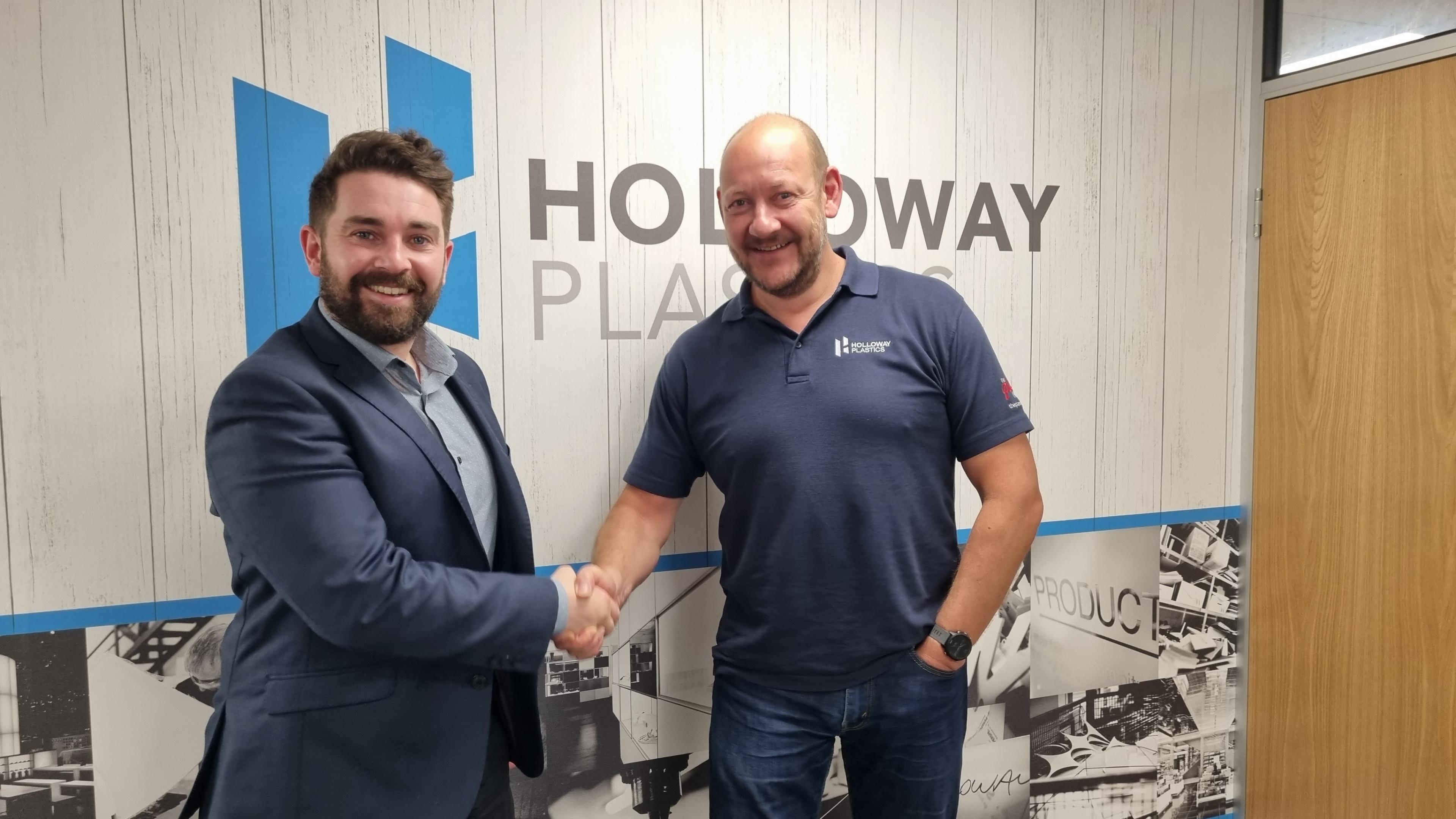 Two men shaking hands in front of a sign that says Holloway Plastics, they are both smiling at the camera