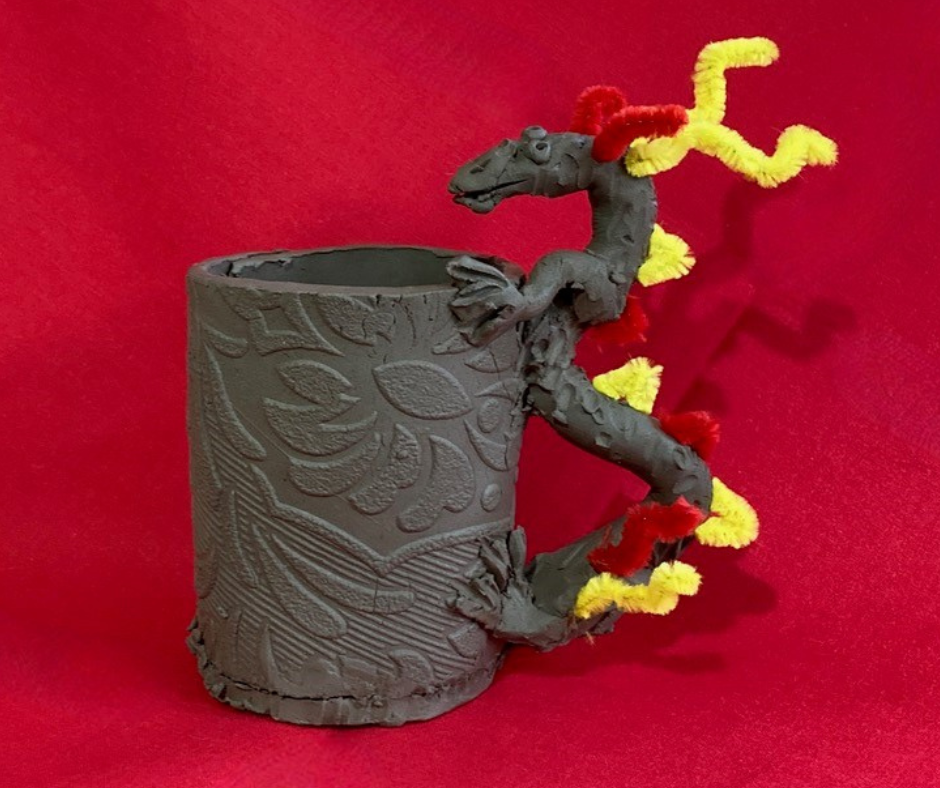 A mug made from clay with a dragon shaped handle.