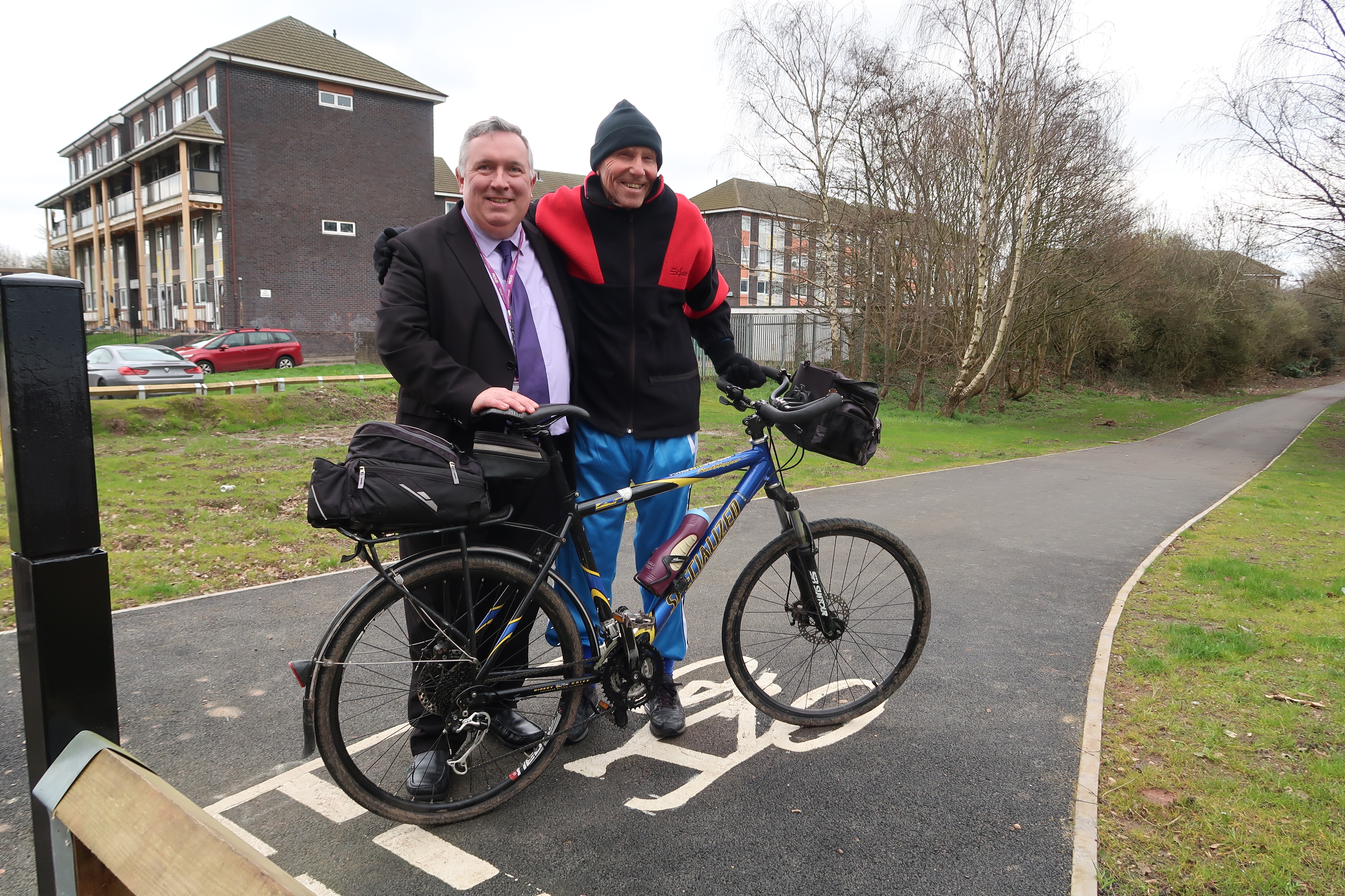 Councillor Adrian Andrew stands next to a cyclist on a cycle path, both smile towards the camera