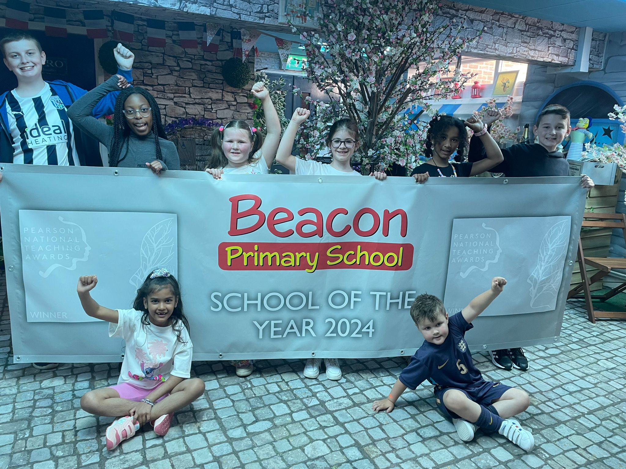 Image depicts children from Beacon Primary School holding a banner to celebrate School of the Year.