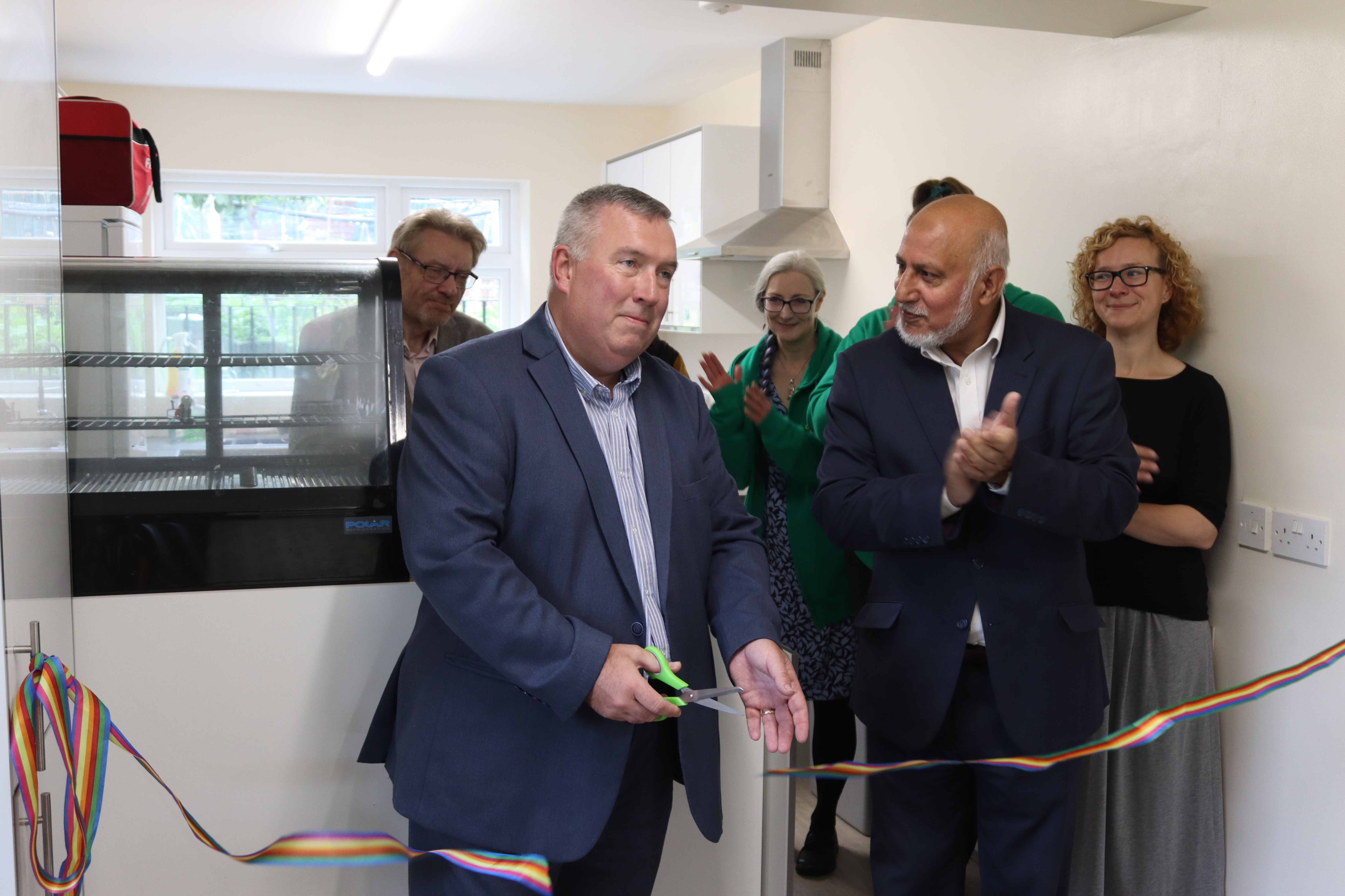 Two men in suits celebrate as they cut a ribbon