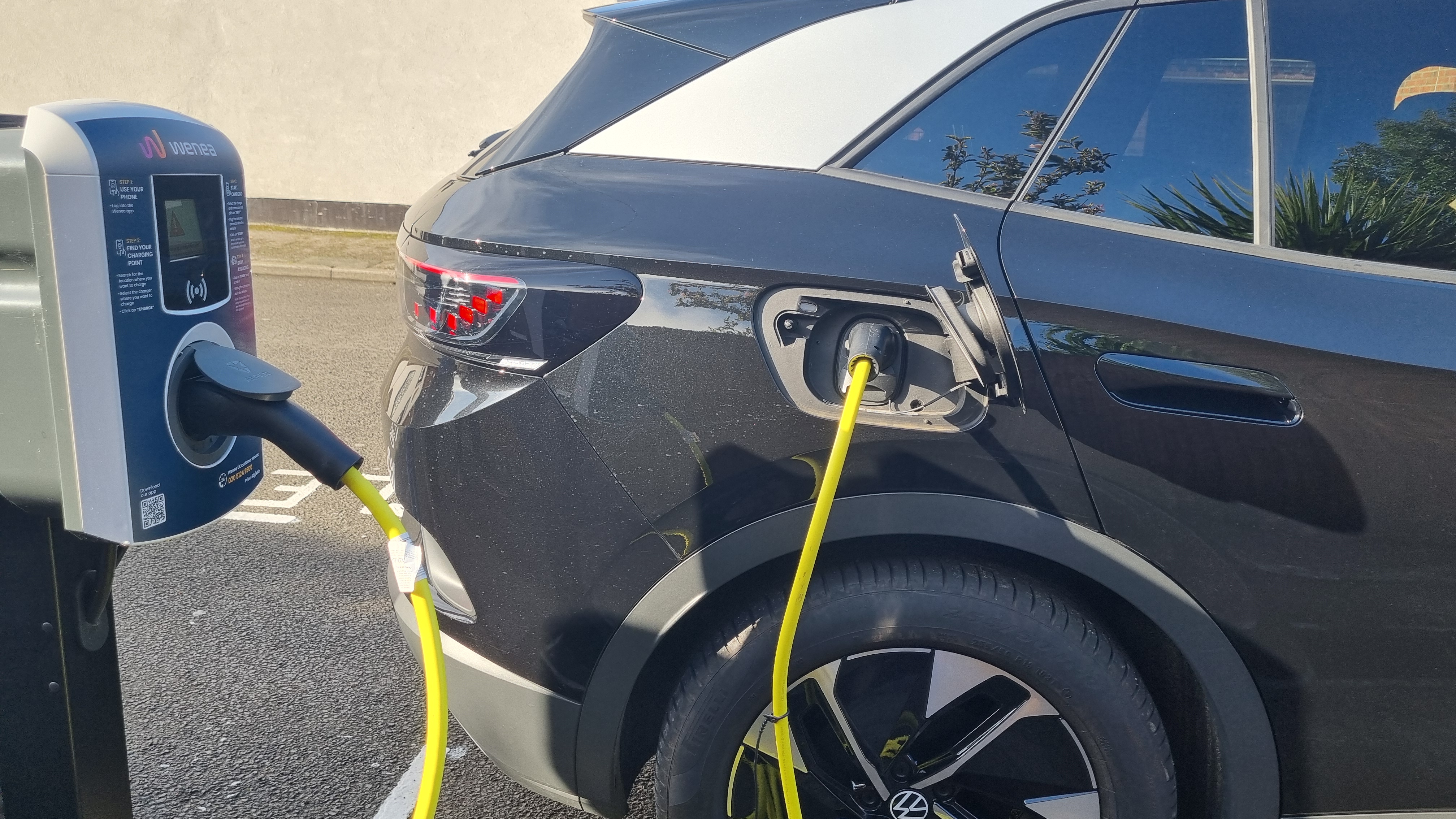 A black vehicle plugged in to an electric vehicle chargepoint by a bright yellow cable