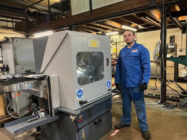 A man in blue stands next to a large piece of machinery