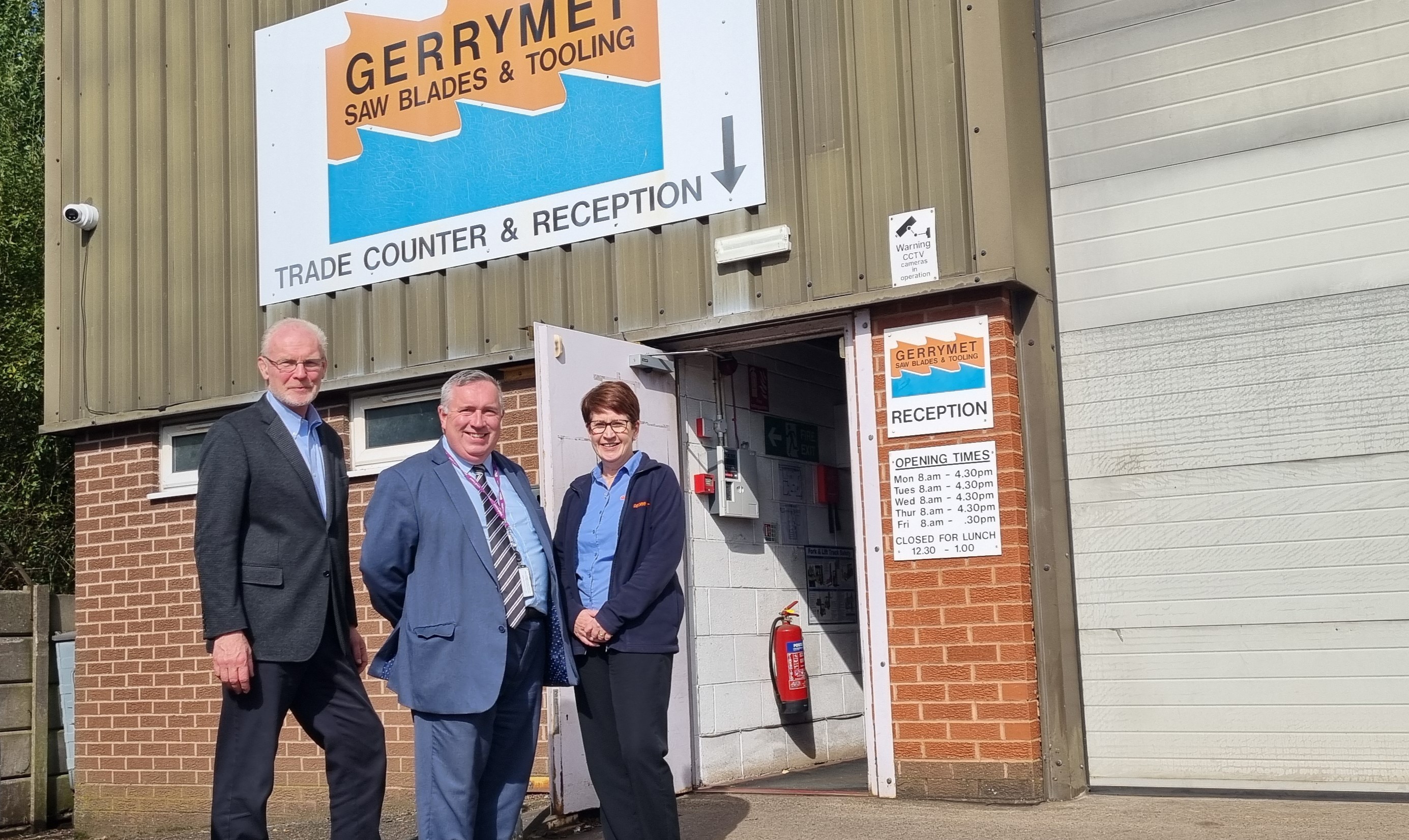 Three people outside the Gerrymet Ltd factory smile at the camera