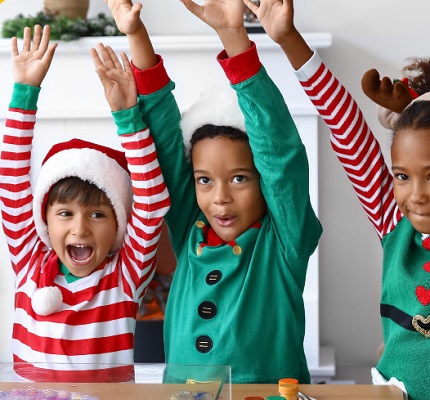 three young children in elf costumes and festive Santa hats with their arms in the air.