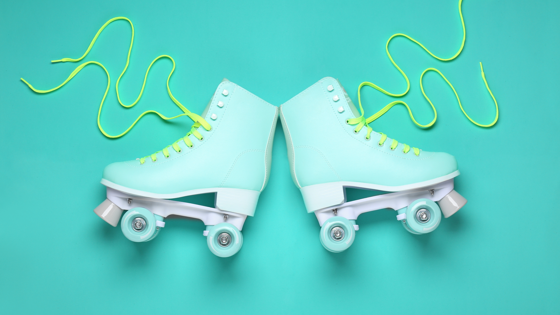 Pale blue roller skates with yellow laces lying flat on a darker turquoise background