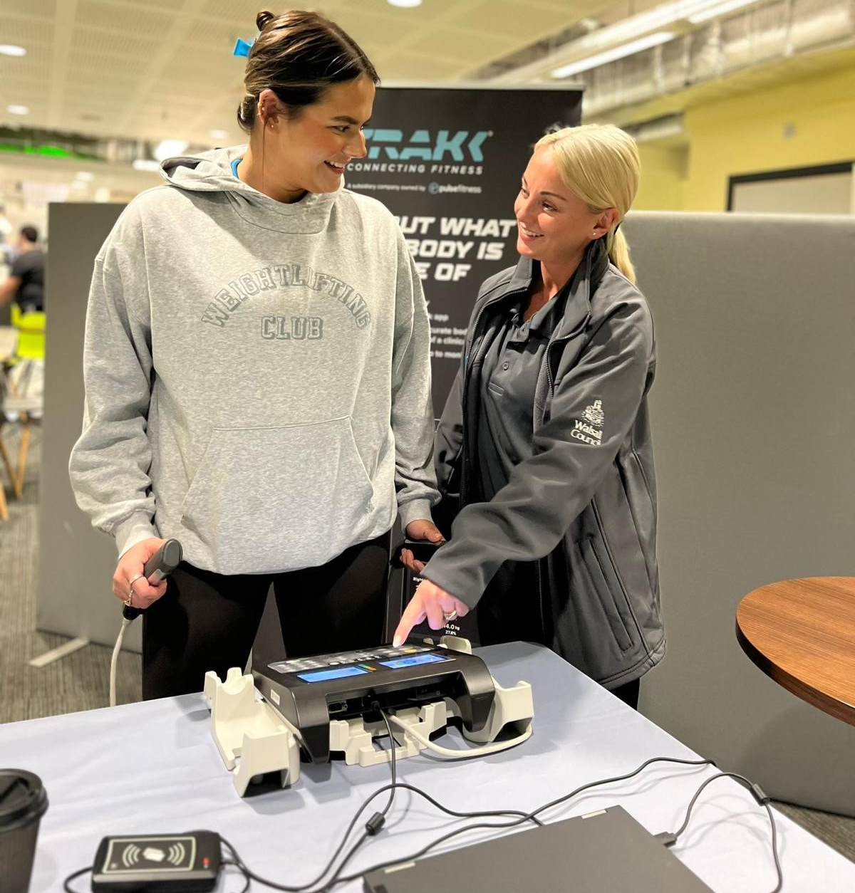 female Instructor guiding a female customer who is standing on scales how to use the equipment in a leisure centre background