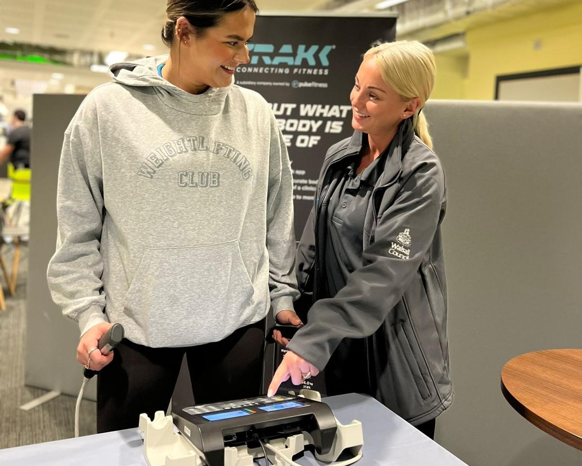 Female instructor standing with a female customer showing how to use a set of scales indoor in leisure centre reception