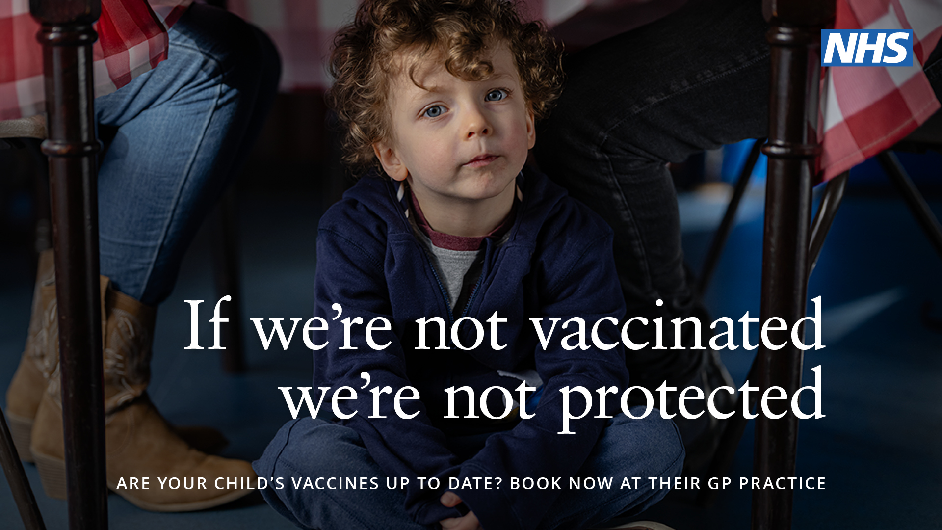 Image depicts a boy under a table. Text: if we're not vaccinated we're not protected.