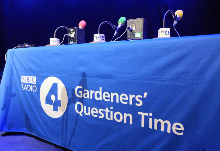 A table covered in a BBC Radio 4 Gardeners' Question Time branded tablecloth as well as microphones for the panel