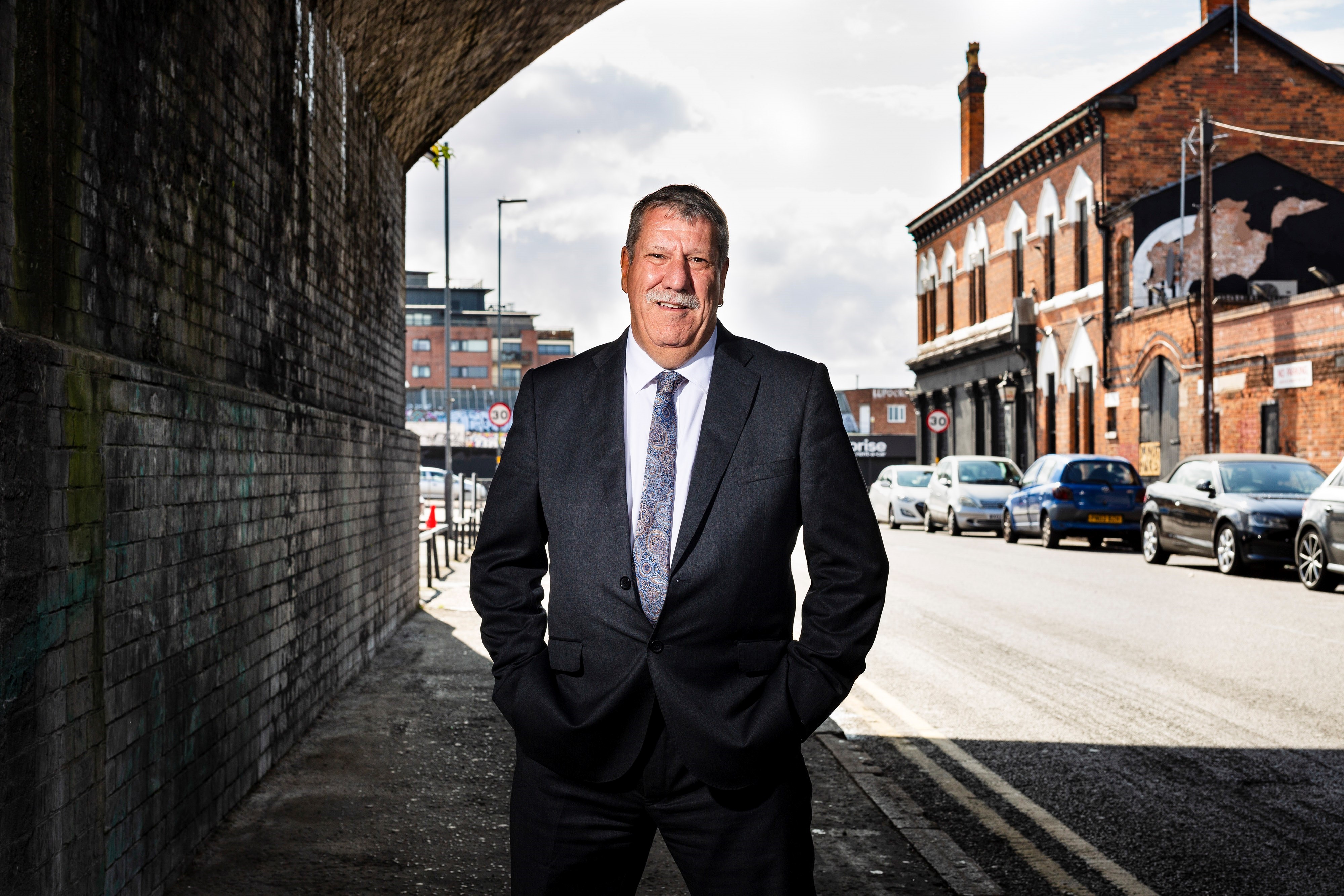 Carl Chinn standing in a tunnel with a brick building behind