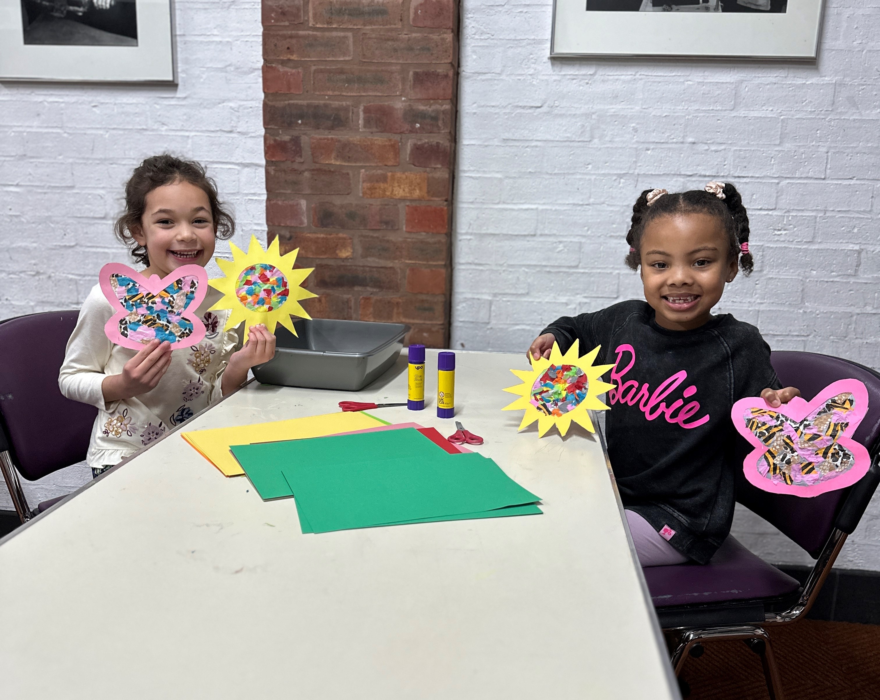 Two young children holding artworks of paper flowers they have made