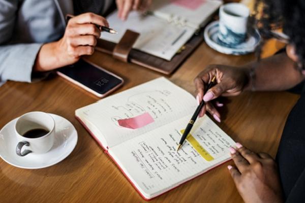 People taking notes at a desk in a meeting