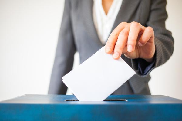 Close up of a person's hand casting their vote in a ballot box