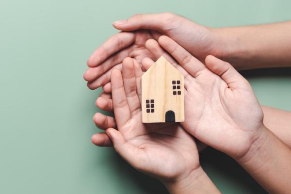 Two pairs of hands holding a small wooden model house