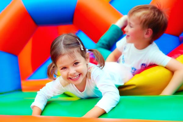 Two children playing on a colourful bouncy castle and smiling