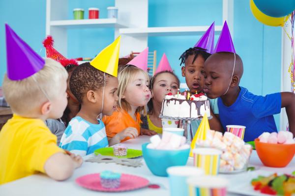 A group of six children wearing party hats and blowing out the candles on a birthday cake