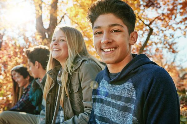 A group of teenagers outside in an autumn setting, facing the camera and smiling.