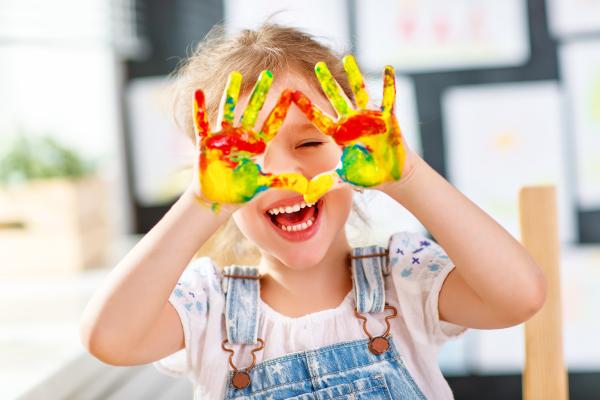 Young girl excitedly laughing, her hands covered in paint