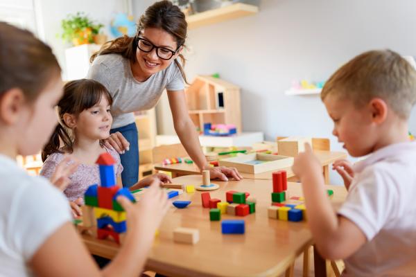 A group of children playing with toy building blocks while a carer smiles over them