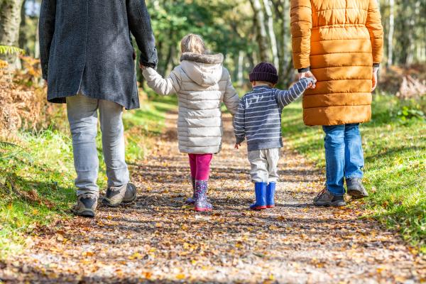 2 adults and two children walking amongst autumnal leaves in a wood