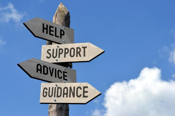 Wooden signpost showing signs for help, support, advice and guidance, with blue sky behind