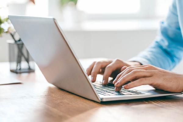 Open laptop on a table with a pair of hands typing on it.