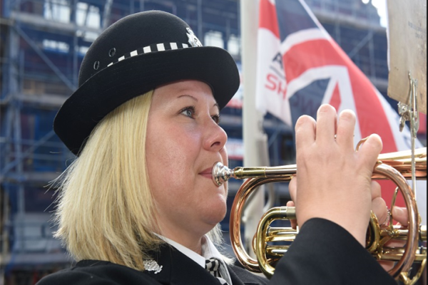Image shows a woman in police uniform playing a fanfare on a brass instrument.