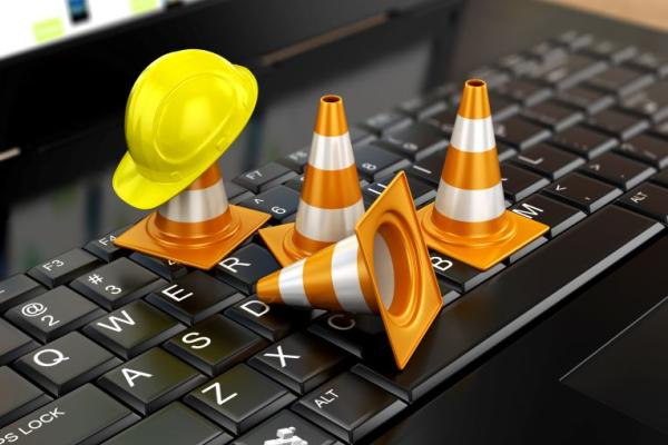 Image shows four orange cones and a yellow maintenance hat on a laptop keyboard.
