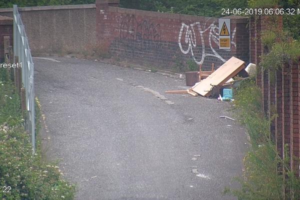 A screenshot of a CCTV image showing a road with fly tipped rubbish dumped to the side
