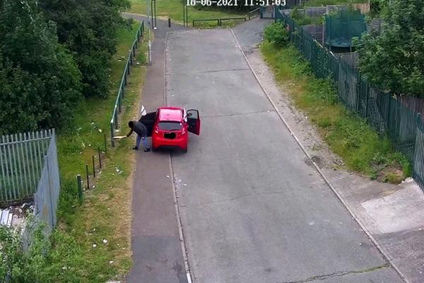 Image shows CCTV footage of fly-tipping by a person in a red car.