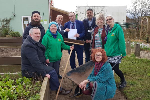 A group of people standing in a community garden smiling at the camera