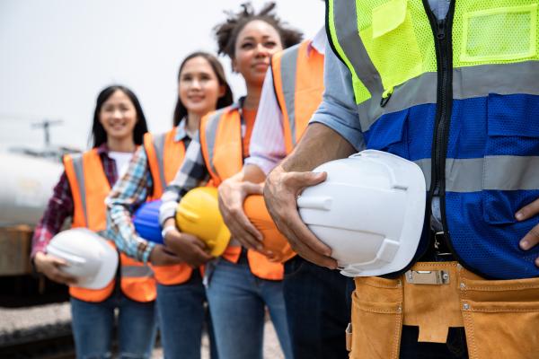 a group of young people in a line wearing high vis jackets and holding hard hats on a construction site