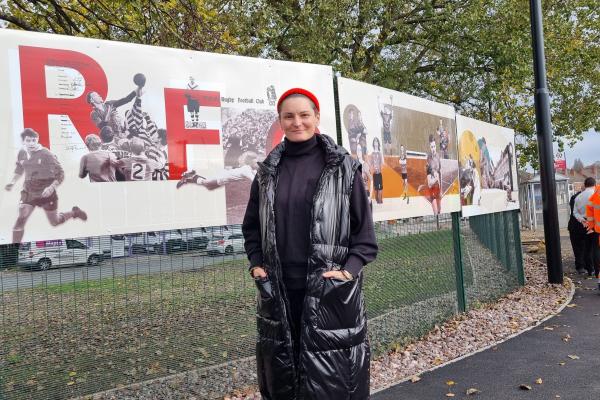 Marta Kochanek of So Good Studio standing in front of a large section of artwork wearing a red had and black coat