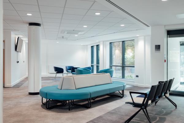 Inside a bright and modern reception area, the walls and ceiling are white and there are turquoise chairs in the middle