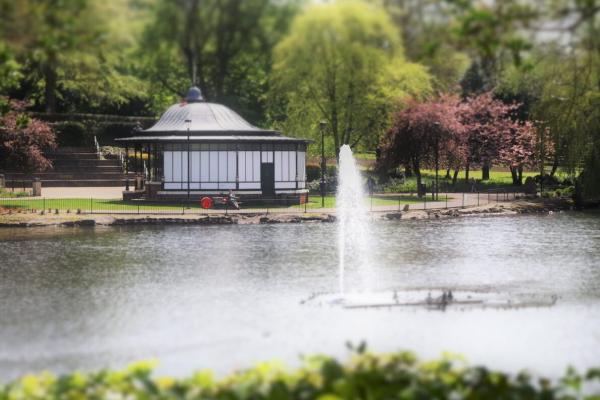 A view of the bandstand in Walsall Arboretum across the lake with a water feature in the lake.