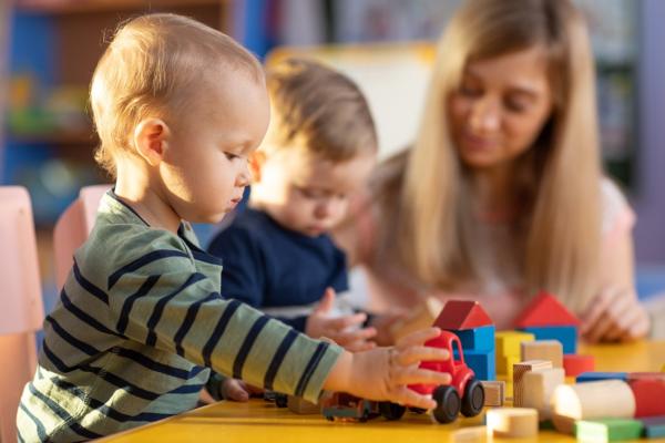 Image depicts two children playing with building blocks with an adult sat with them.