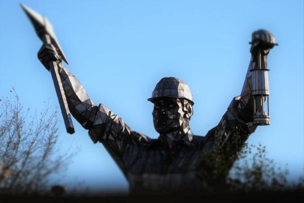 Metal sculpture of a miner holding a pick axe and a mining lamp aloft.